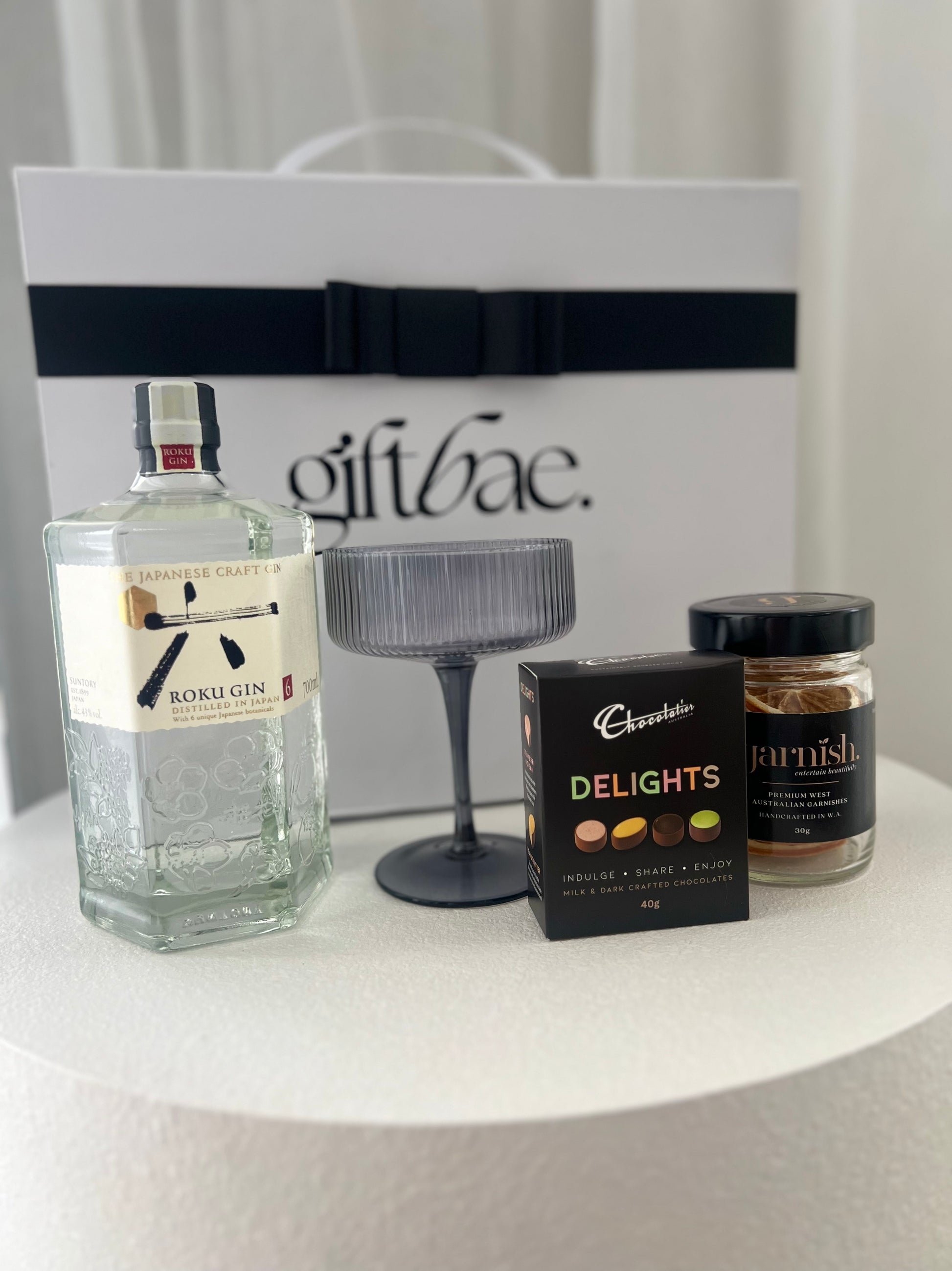 Bottle of Roku Gin, a box of chocolates, and a jar of snacks on a table with a 'giftbae' box in the background. Sip Sip Gin Box | Luxury gift hampers Australia – beautifully curated gourmet hampers, wine gift boxes, and pamper hampers for all budgets. Perfect for birthdays, anniversaries, corporate gifts & special occasions. Gift Bae offers Perth same-day delivery & Australia-wide shipping. Shop the best gift hampers online today!