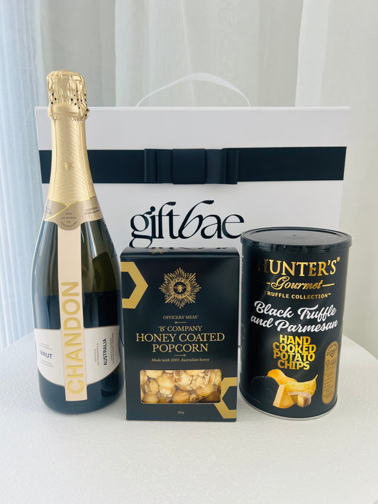 Bottle of Chandon champagne, box of honey-coated popcorn, and can of black truffle potato chips with a 'giftbae' branded bag.| Luxury gift hampers Australia – beautifully curated gourmet hampers, wine gift boxes, and pamper hampers for all budgets. Perfect for birthdays, anniversaries, corporate gifts & special occasions. Gift Bae offers Perth same-day delivery & Australia-wide shipping. Shop the best gift hampers online today!